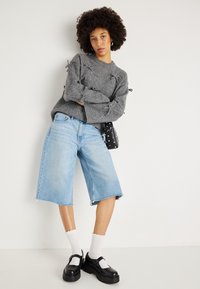 Pilkas mezginys su dekoratyvinėmis kaspinu, šviesiai mėlyni džinsiniai bermudai, balti banguoti kojinai ir juodi platforminiai bateliai.