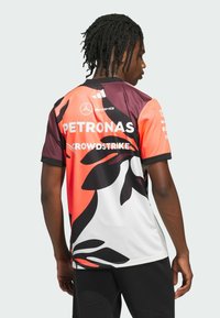 Maglia a maniche corte di colore arancione, nero e bianco con motivi astratti. I loghi includono Petronas e Crowdstrike. Realizzata in materiale leggero.
