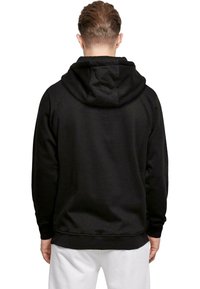 Felpa nera con cappuccio e design semplice, dotata di tasca a marsupio e polsini a coste. Il materiale sembra morbido e strutturato.