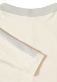 Vaalea kermaisen värinen kangas, jossa on tasainen rakenne ja kontrastoiva harmaa ribbineck. Ominaisuuksiin kuuluu rento istuvuus ja hienovarainen sauman yksityiskohta hihassa.