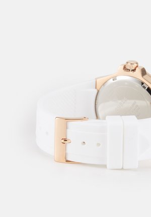 Hvit silikon klokkerem med gullfarget metallspenne, med en glatt tekstur og et rundt, metallisk klokkehus med en krone.