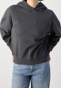 Tmavě šedá mikina s výšivkou loga "Marc O'Polo", volný střih, dlouhé rukávy a žebrovaný lem. Nosená přes světle modré džíny.