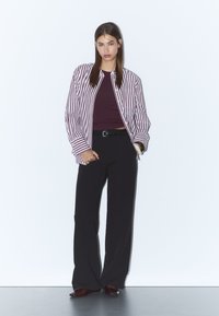 Randig långärmad skjorta i röd och vit över en åtsittande mörk topp, matchad med svarta vida byxor. Accessoarer med ett svart bälte.