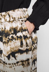 Pantaloni con motivo che presentano un design astratto bianco, oro e nero, con una cintura elastica e tasche laterali. La texture sembra morbida.