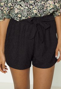 Černé šortky s elastickým pasem a detailem vázané mašle. Tkanina má texturovaný otvorený vzor, což zajišťuje lehký pocit.
