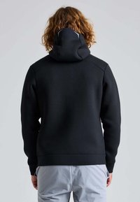 Haut à capuche noir avec un col montant et une capuche réglable. Fabriqué en tissu doux, il présente une texture lisse et des poignets côtelés. Vue arrière montrée.