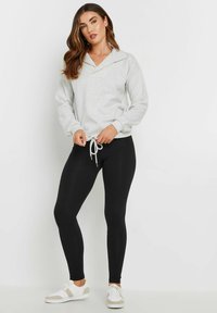 Felpa grigia con colletto a scialle e orlo con coulisse, abbinata a leggings neri e sneakers bianche con dettagli grigi.
