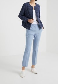 Laivastonsininen teksturoitu takki, jossa on lyhyt muotoilu, yhdistettynä vaaleansinisiin räätälöityihin housuihin ja valkoisiin korkokenkiin. Yksinkertainen valkoinen toppi sen alla.