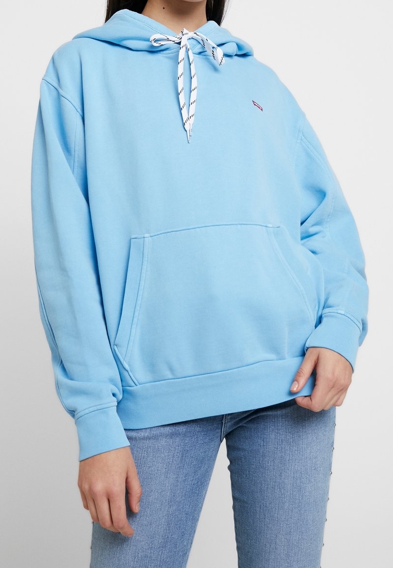 Jasnoniebieska bluza z kapturem wykonana z miękkiego materiału, z przednią kieszenią, ściągaczami na mankietach i wzorzystym ściągaczem w kapturze.