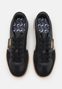 Baskets noires en cuir et en daim avec une semelle en caoutchouc beige, des accents texturés et une semelle intérieure à motifs arborant le logo Puma.