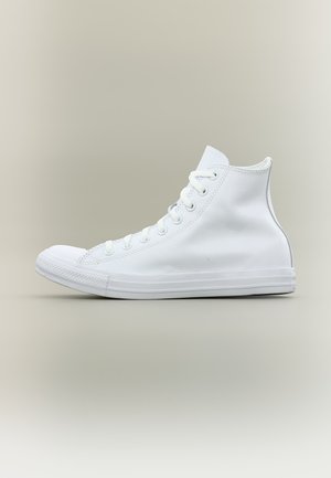 Zapatilla blanca de caña alta con cordones, puntera de goma y suela plana, mostrada sobre un fondo gris claro liso.