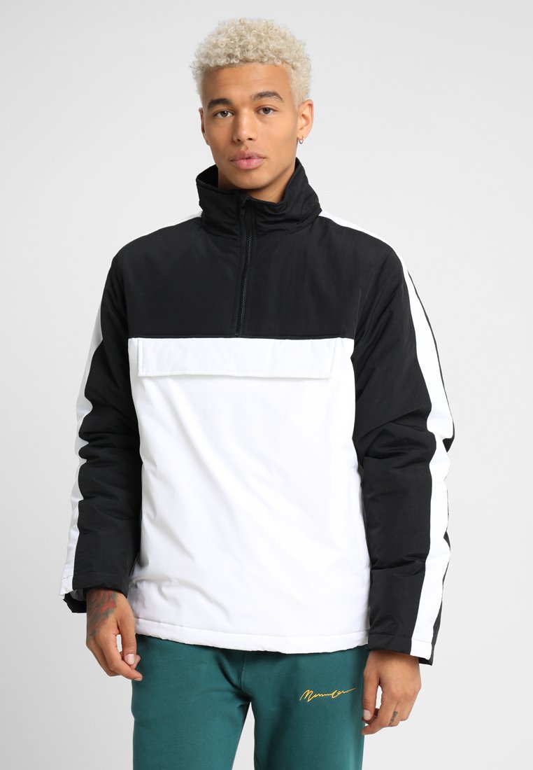 Half-zip pullover laget av et slitesterkt stoff, med en svart toppseksjon, hvit kropp og sidestriper, samt høy krage.