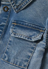 Tessuto in denim blu chiaro con un design dettagliato della tasca. Cuciture visibili in un colore a contrasto, superficie testurizzata e aree sbiadite creano profondità.