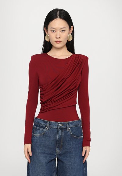 Haut à manches longues bordeaux avec des détails froncés, associé à un pantalon en denim bleu taille haute. Texture lisse, design ajusté à la taille.