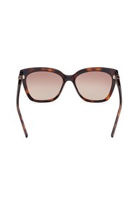 Lunettes de soleil en écaille de tortue avec une large monture géométrique, des verres dégradés et des branches fines dotées d'accents en argent au niveau des charnières.