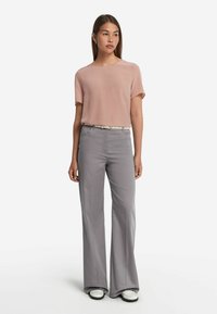 Ljusrosa kortärmad blus ihop med grå skräddarsydda byxor. Byxorna har en utsvängd skärning och ett standard midjeband, kompletterat med ett ljust bälte.