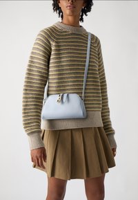 Tynn, lys blå skinncrossbody-veske med gullhardware, med rund form og glidelås. Stripete strikkegenser og plissert skjørt.