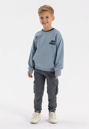 Lichtblauwe sweatshirt met een zak aan de voorkant en de tekst "ATH CREW" in het zwart, gecombineerd met grijze cargo-broeken en witte sneakers. Eenvoudig ontwerp.