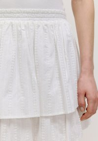 Witte gelaagde rok gemaakt van gestructureerde stof met verticale strepen en draadaccenten; elastische tailleband; gelaagd ontwerp.