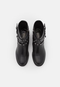 Botas de tobillo de cuero negro con tachuelas metálicas y correas. Textura suave, punteras redondeadas y suelas planas. Etiqueta de la marca visible en el interior.