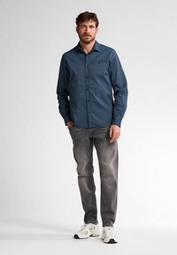 Blauw geruit overhemd met knopen en een brede kraag, gecombineerd met grijze jeans en witte sneakers. Het overhemd heeft een borstzak en een subtiele textuur.