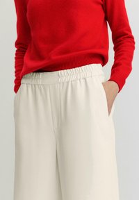 Rode gebreide trui met een geribbelde boord, gecombineerd met crèmekleurige comfortabele broek met een elastische tailleband en zijzakken.