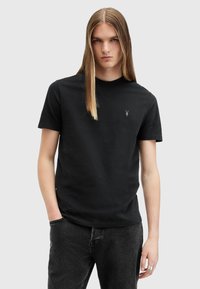 Sort bomulds t-shirt med rund hals, korte ærmer og et broderet logo på brystet, parret med mørke jeans. Glat tekstur.