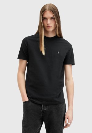 Svart bomull T-skjorte med rund hals, korte ermer, og en brodert logo på brystet, sammen med mørke jeans. Glatt tekstur.