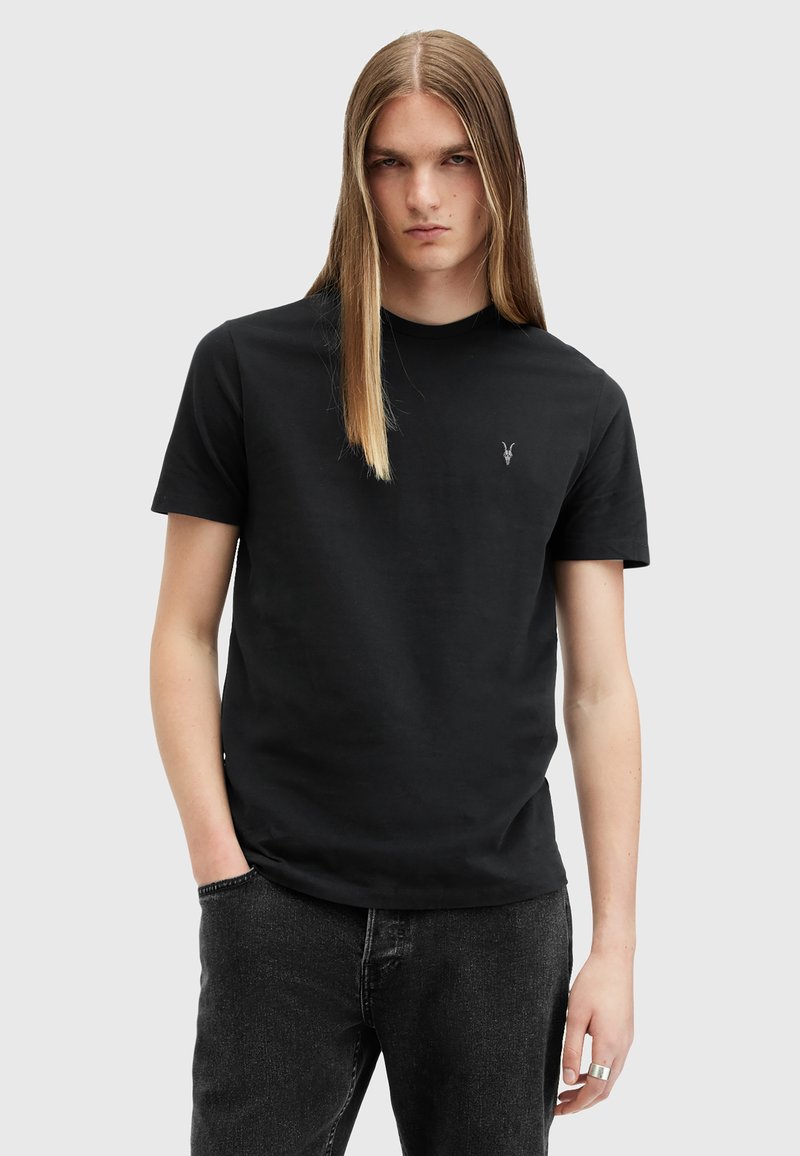 Sort bomulds t-shirt med rund hals, korte ærmer og et broderet logo på brystet, parret med mørke jeans. Glat tekstur.