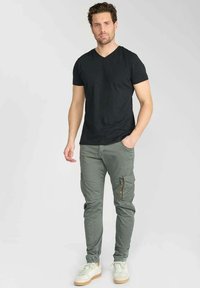 Zwarte v-hals t-shirt gecombineerd met groene cargo broek met zijzakken en ritsen, aangevuld met witte sneakers. Glad materiaal en een aansluitend ontwerp.