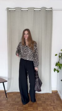Blusa de manga longa com padrão de leopardo, combinada com calças largas de cintura alta, pretas. Bolsa castanha escura de textura suave.
