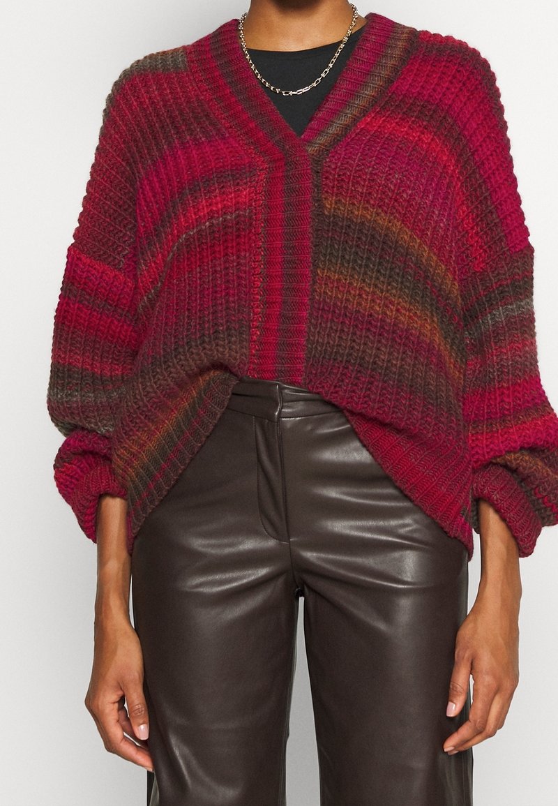 Chunky stickad tröja med V-ringning, med röda och bruna ränder. Ribbad textur, oversized ärmar, kombinerad med bruna läderbyxor.