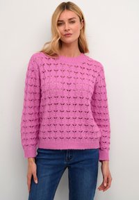 Maglione rosa lavorato a maglia con un motivo traforato testurizzato, scollatura rotonda e maniche lunghe, abbinato a jeans blu.