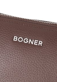Rjava usnjena torba z teksturirano površino, ki vsebuje srebrno znamko "BOGNER" in zadrgo ob zgornjem robu.