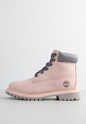 Bottine rose clair montant à la cheville avec col matelassé gris, lacets noirs, semelle robuste et logo Timberland sur le côté, sur fond uni.