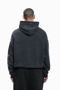 Dark gray cropped hoodie with a large hood, loose fit, and ribbed cuffs. Features a graphic design on the left sleeve. Soft texture.