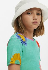 Grön ribbad t-shirt med färgglada broderade blommor och fjärilar på ärmarna, rund halsringning och rosa detaljer.