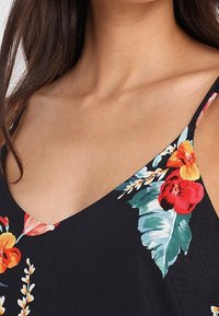 Czarny top na ramiączkach z żywymi wzorami kwiatowymi w odcieniach czerwieni, pomarańczu i zieleni. Ramiączka spaghetti oraz głęboki dekolt w kształcie litery V. Gładka tekstura materiału.