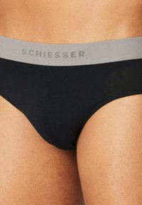 Schwarze Baumwollunterhose mit einem grauen elastischen Bund, der das "SCHIESSER"-Logo in einem sich wiederholenden Muster trägt. Glatte Textur und figurbetontes Design.