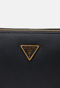 Czarny portfel z fakturowanej skóry ekologicznej z złotym trójkątnym logo Guess USA oraz złotym zamkiem błyskawicznym. Charakteryzuje się eleganckim designem i subtelnymi detalami.