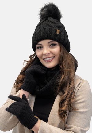 Beanie a maglia nera con pompon, guanti coordinati e una sciarpa texturizzata, tutti caratterizzati da un colore nero uniforme e elementi di design accoglienti.