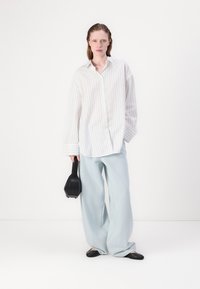 White button-up shirt with light vertical stripes, loose fit, wide light blue pants, black flat shoes, and a small black handbag.