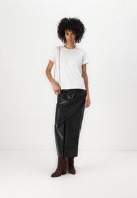 Hvid bomulds T-shirt parret med en sort faux læder midi-nederdel med slids foran. Brune hæle støvler og en lille lyserød taske fuldender looket.