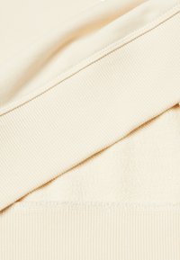 Tessuto color crema, con una texture a coste sullo strato superiore e un interno morbido e peloso, con cuciture pulite e senza hardware visibile.