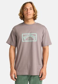Šedé tričko s krátkým rukávem, na přední straně s retro grafikou v tyrkysové barvě "Billabong Australia". Vyrobeno z měkké bavlny.