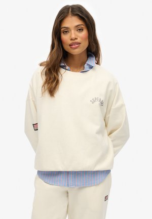 Crème sweatshirt met verlaagde schouders en "Superdry" logo; gelaagd over een lichtblauw en roze gestreept overhemd met kraag. Standaard pasvorm.