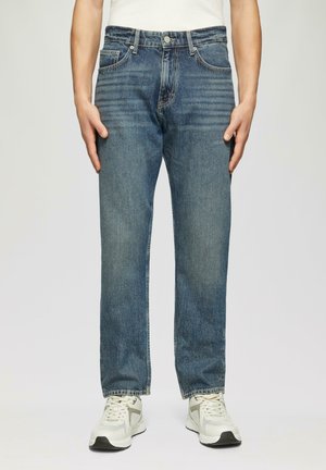 Heren blauwe denim jeans, recht model, medium was, vijf zakken, metalen knoop en ritsluiting, gecombineerd met witte en grijze sneakers.