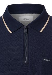 Marineblaues Zip-Polohemd mit einem strukturierten Muster, ausgestattet mit einem cremefarbenen Kragen und einer kleinen Tasche mit einem Logo.