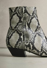 Fekete és szürke kígyómintás bokacsizma, textúrált felszínekkel, alacsony tömbsarkú és testhezálló kialakítással.