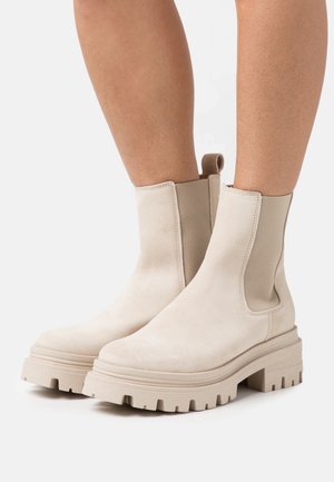 Beige mockaboots till ankeln med elastiska sidopaneler, chunky sula och dragsko. Har en slät textur och rundad tådesign.